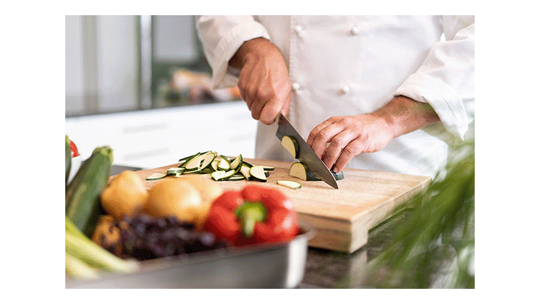 Koch in weißer Jacke schneidet Gemüse auf einem Holzbrett